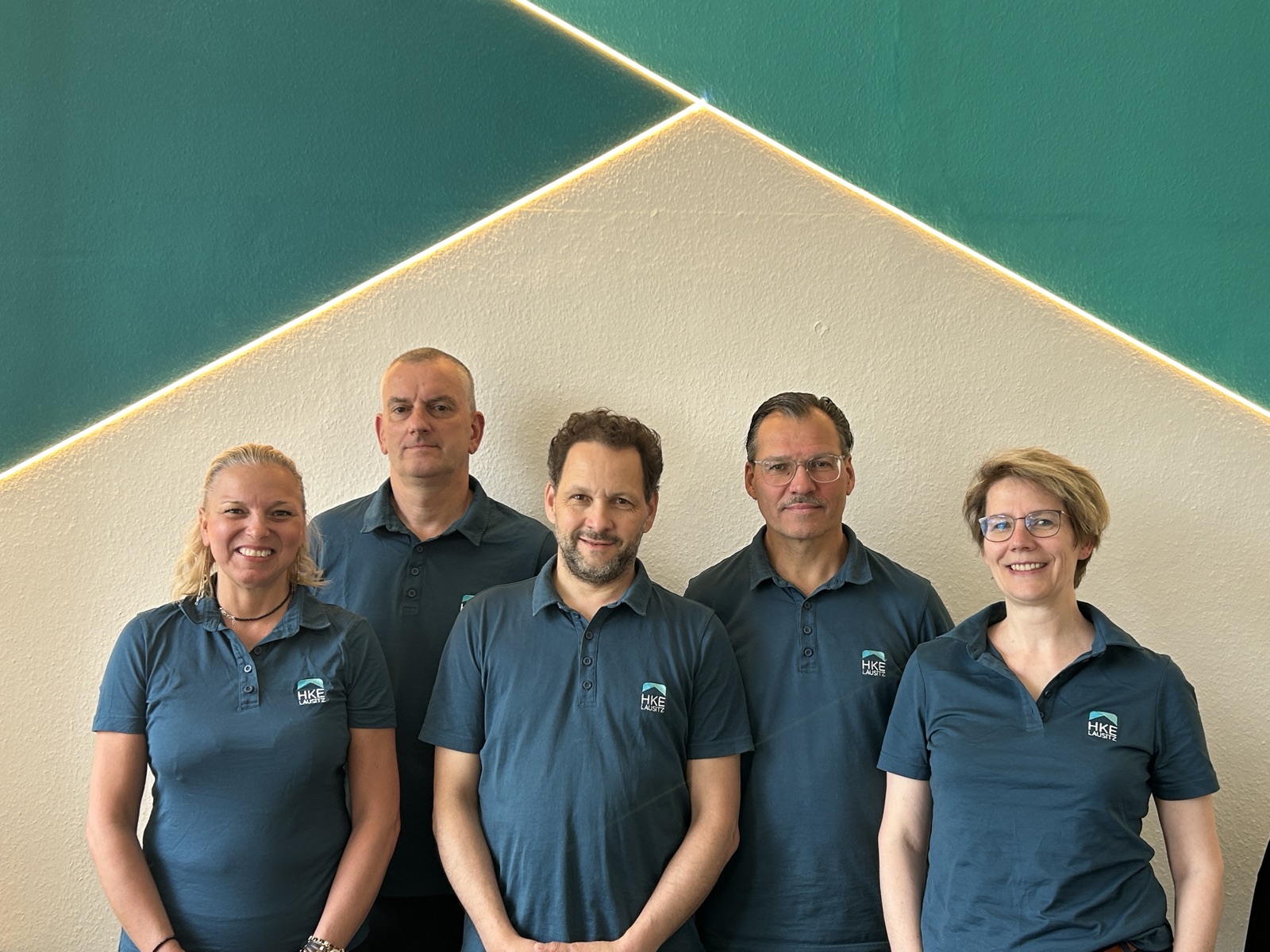 Das HKE-Team in der Lausitz: Mit­arbeitende vor der Teal-Wand im Büro.